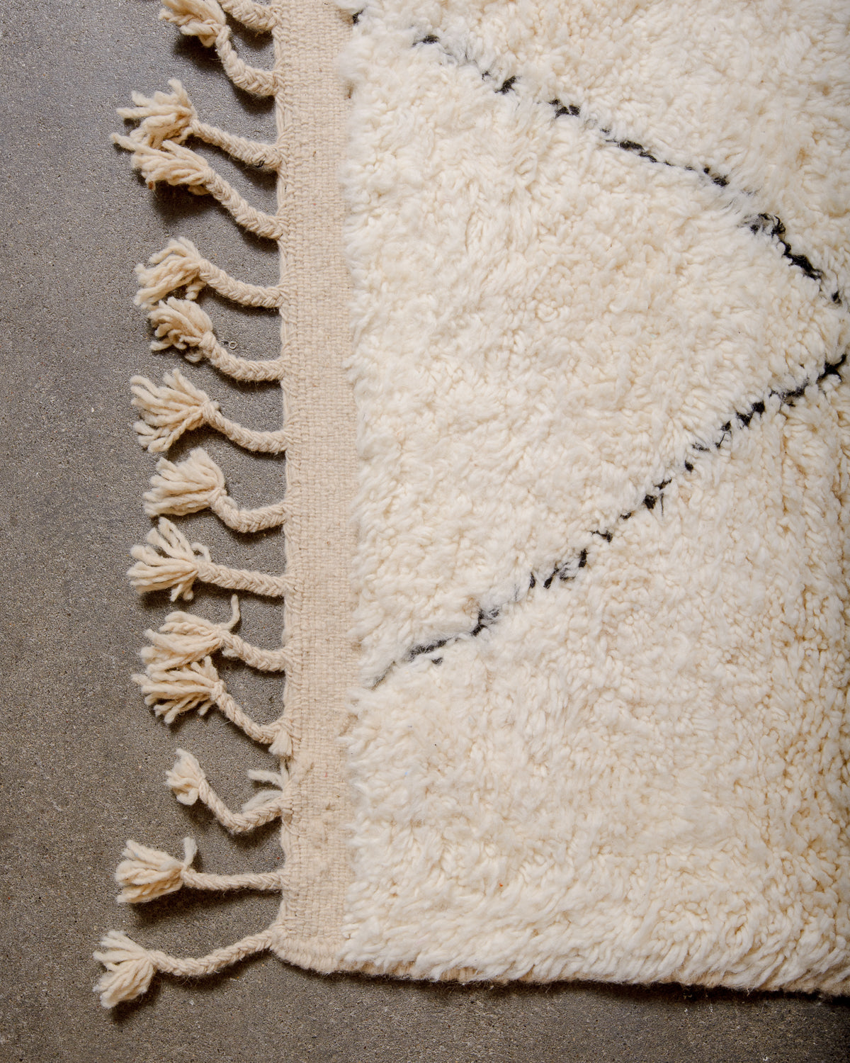 Corner of cream Beniourain rug with black diamond design and natural wool tassels.